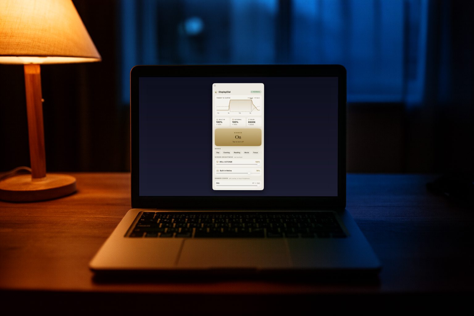 A MacBook on a desk in a dim home office at night, warm lamp glowing nearby, its screen comfortably dimmed by the Daily Dimmer instead of glaring in the dark